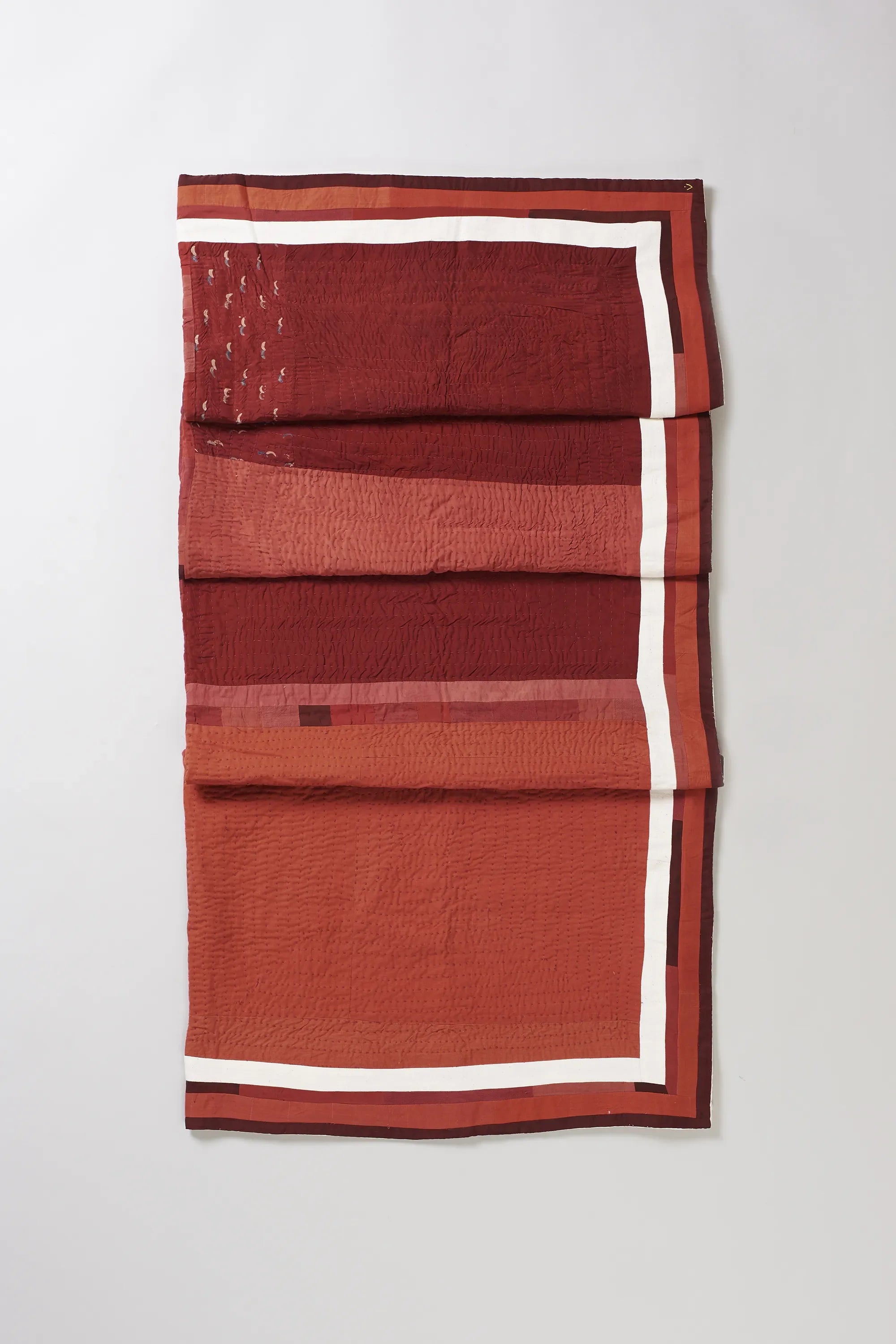 Folded red quilt with white border on a light grey background