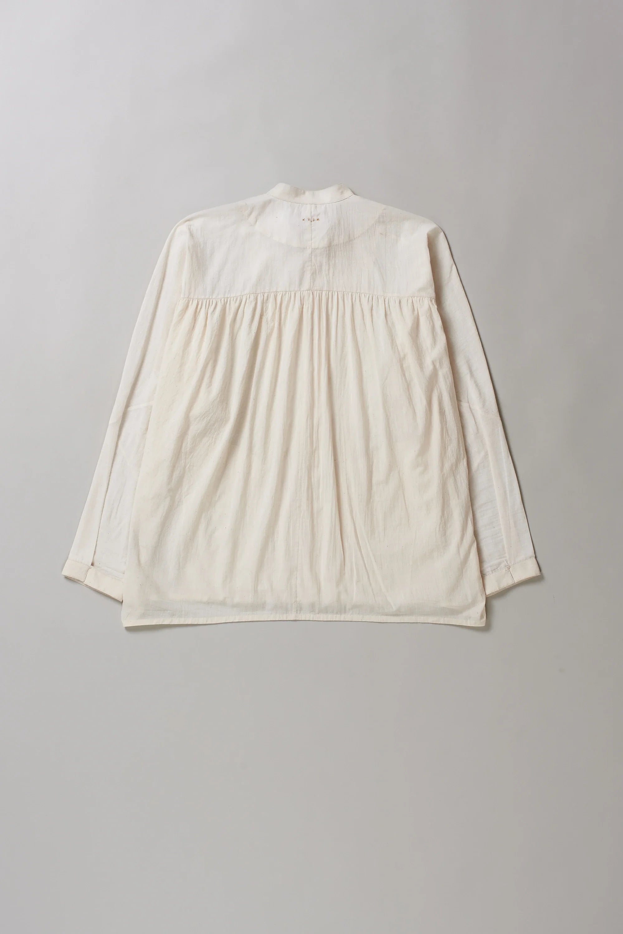 Back image of ecru cotton shirt with hand detailing on a grey background