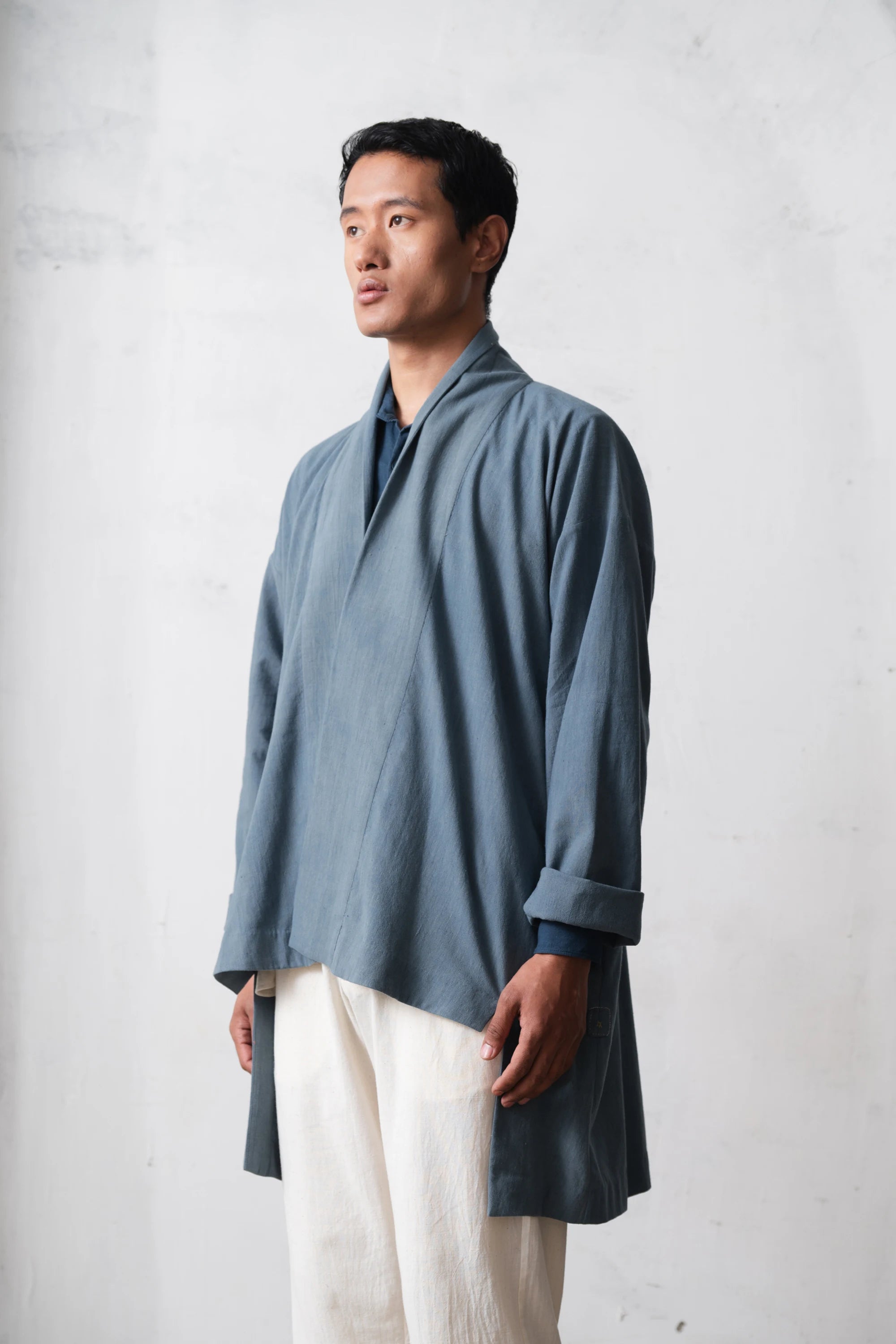 Man wearing a long, light blue shacket with rolled-up sleeves against a light grey background