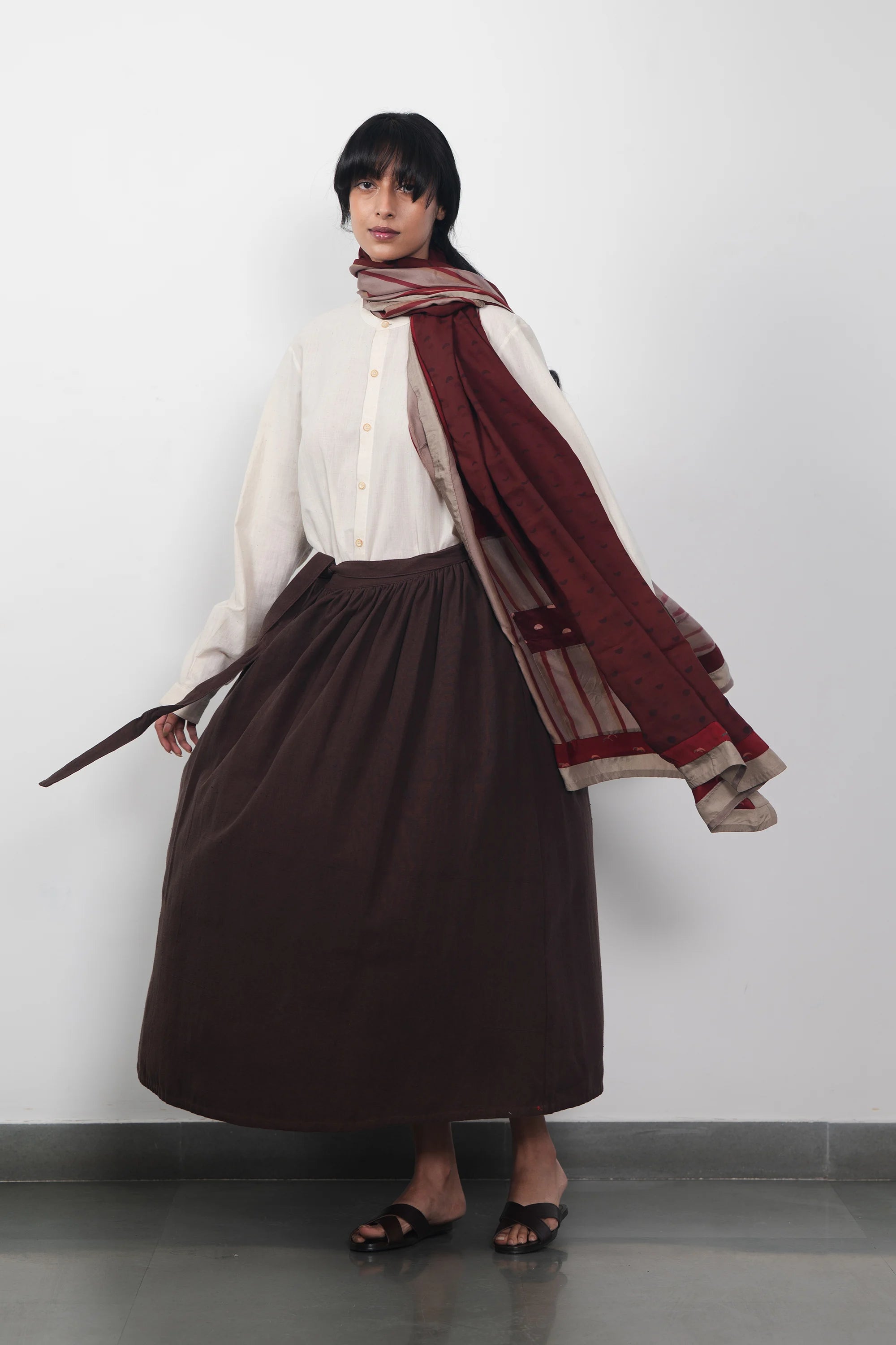 Woman wearing a white shirt, burnt umber skirt, and red scarf against a light grey background