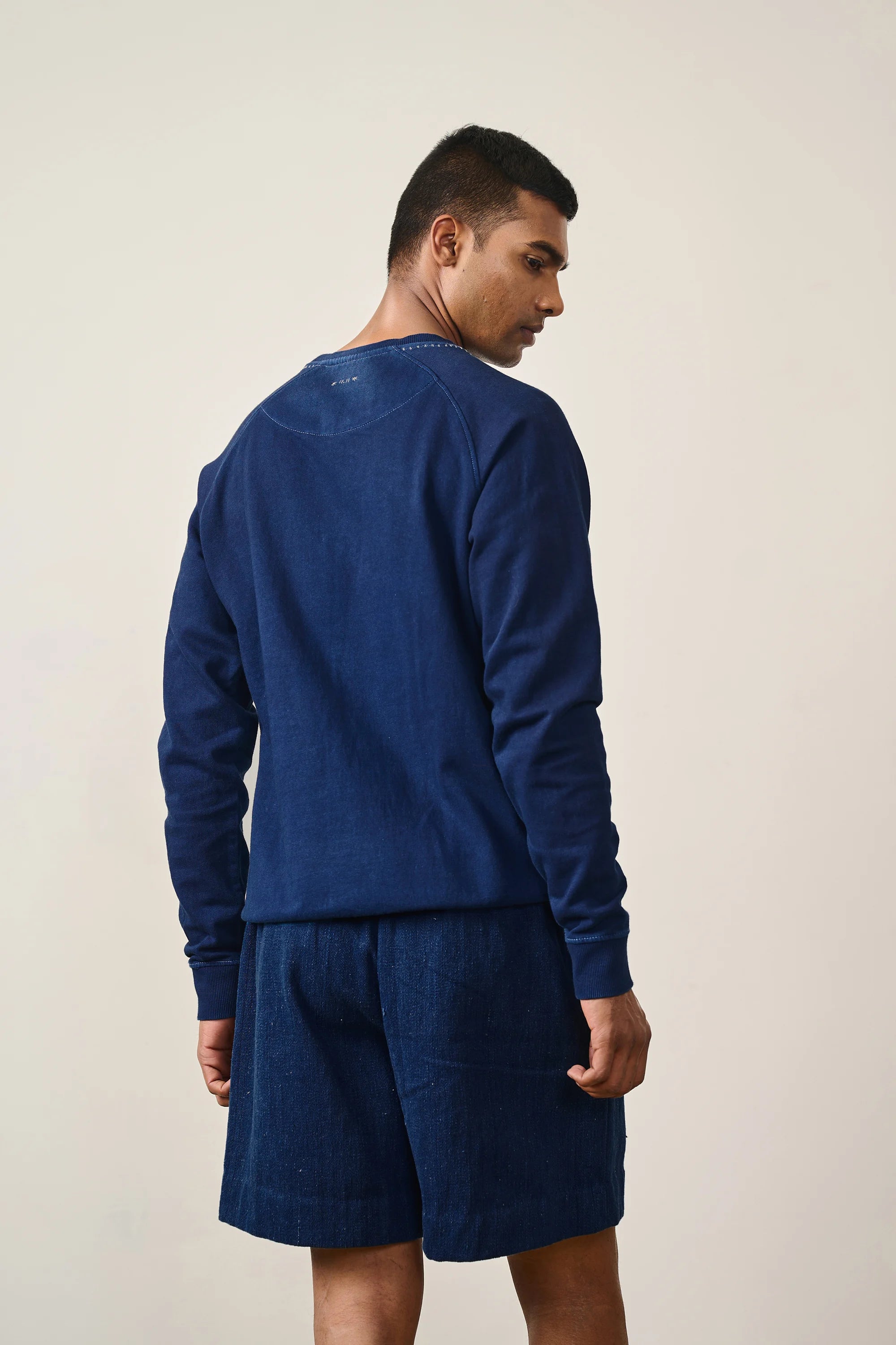 A back shot of a man wearing indigo sweatshirt