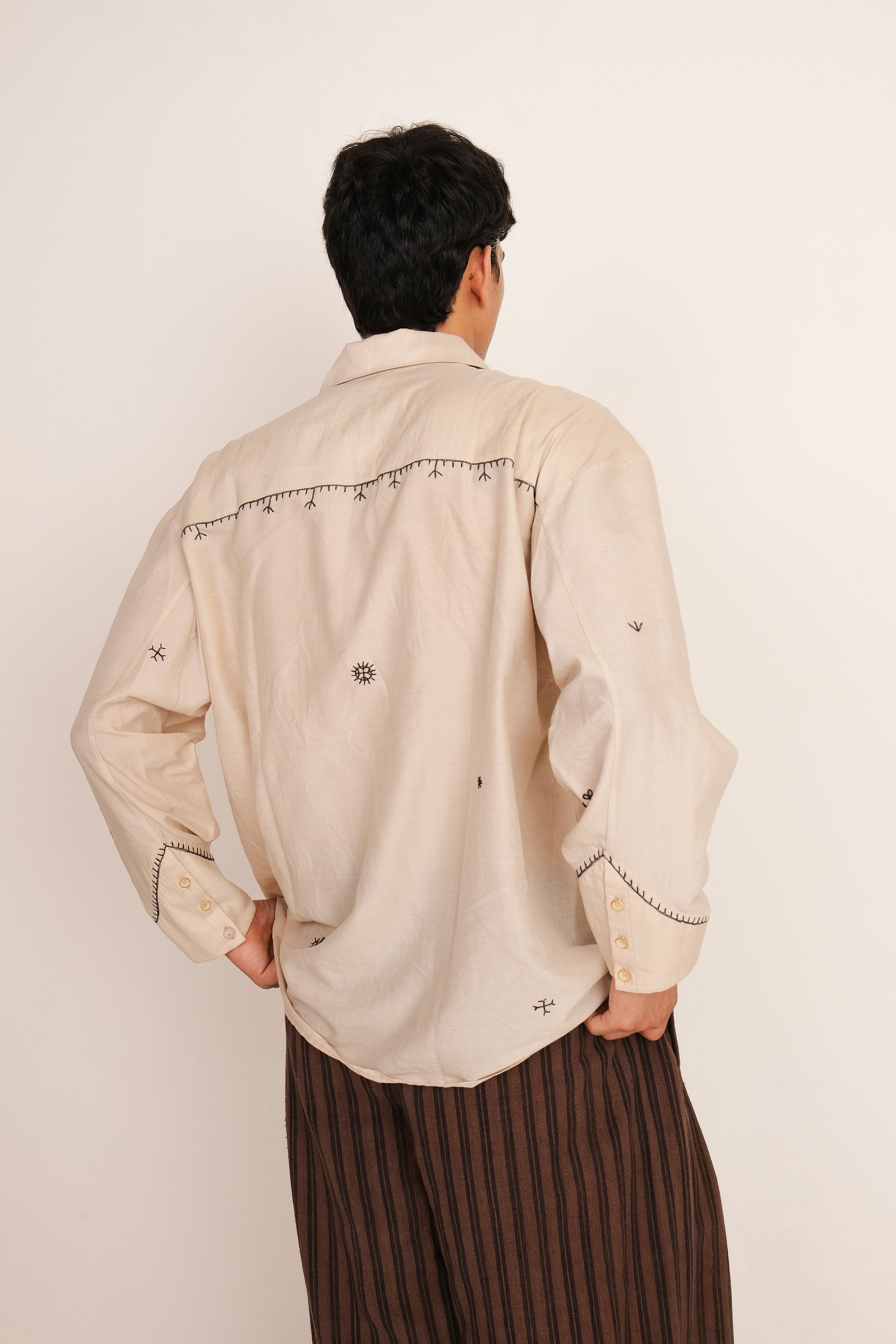Back shot of man wearing a Ecru shirt and burnt umber striped pants against a white background
