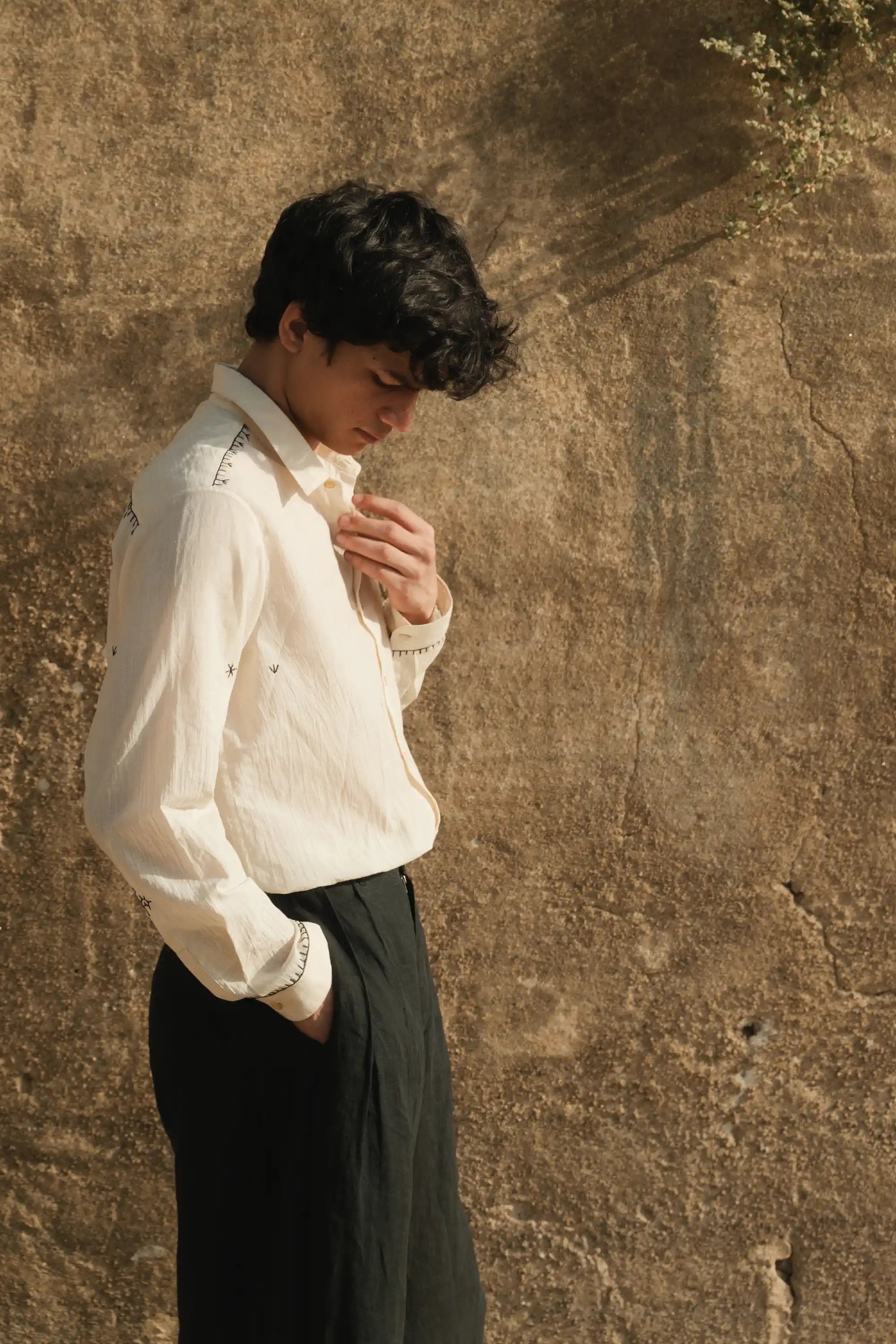 A side shot of a man wearing a black cotton pant with hand embroidery ecru cotton shirt