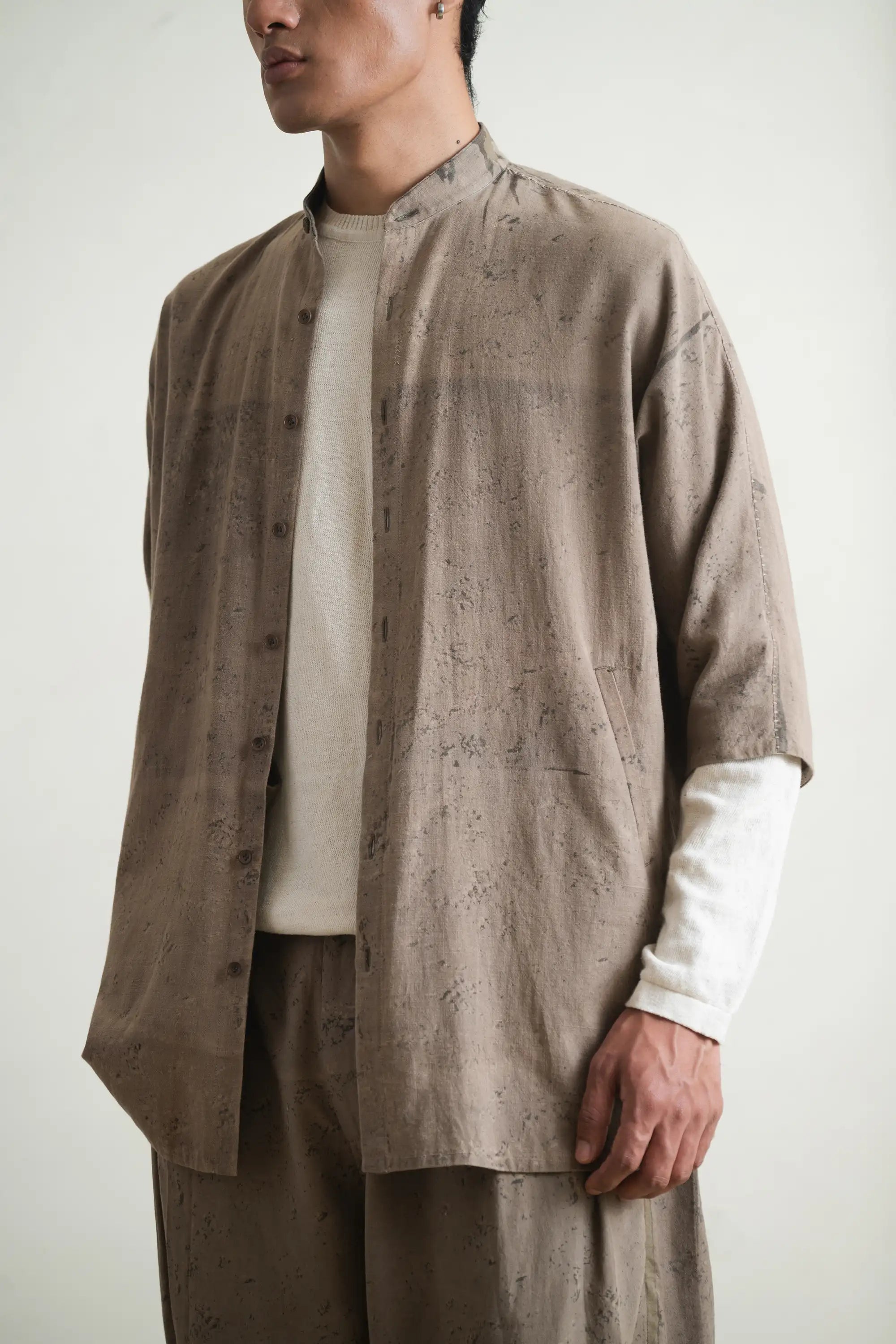 Person wearing a beige textured shirt over a white shirt with beige pants against a light grey background