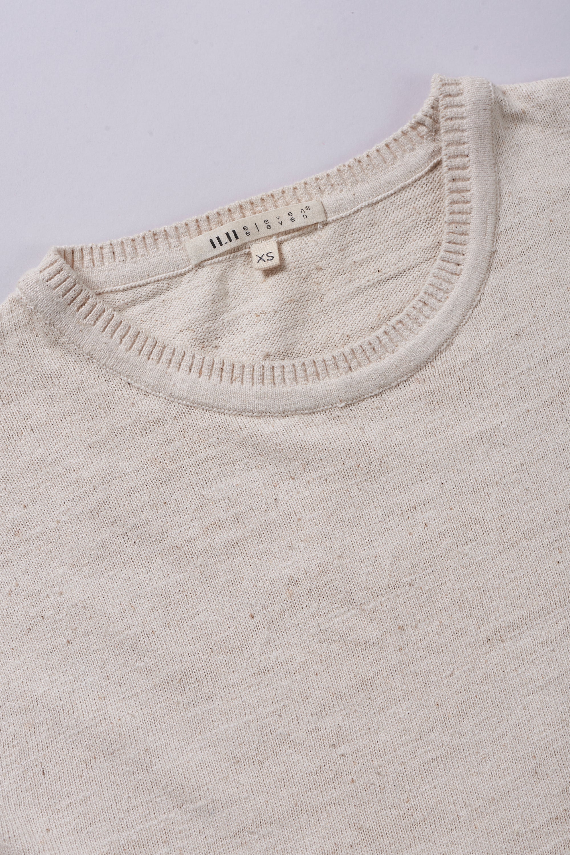 Close-up of a ecru t-shirt with a brand label on a light grey background
