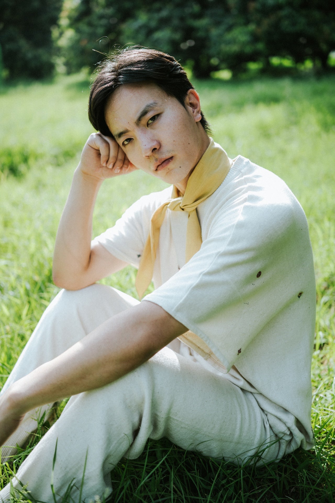 Person sitting on grass wearing a white shirt and yellow scarf