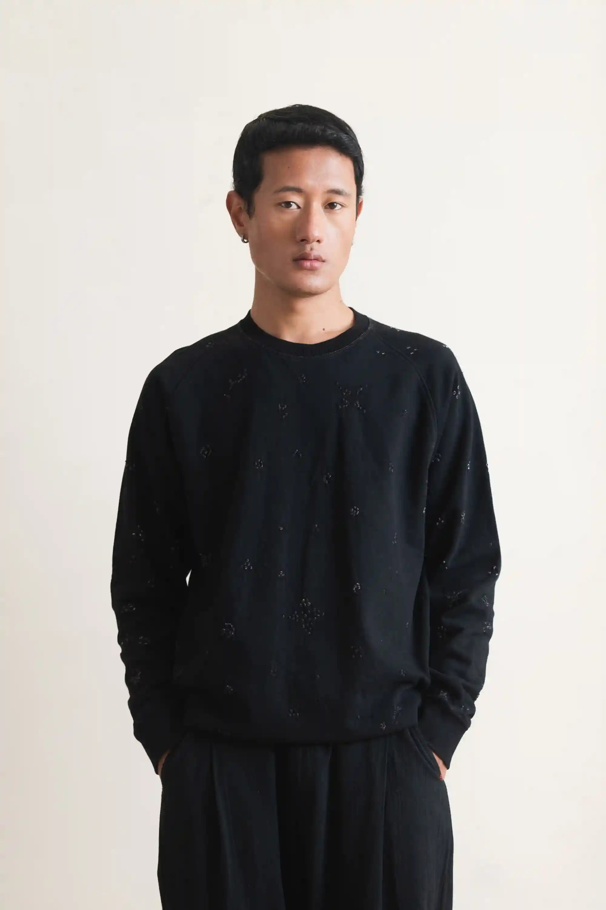 Man wearing a black patterned shirt over a yellow collared shirt against a plain background