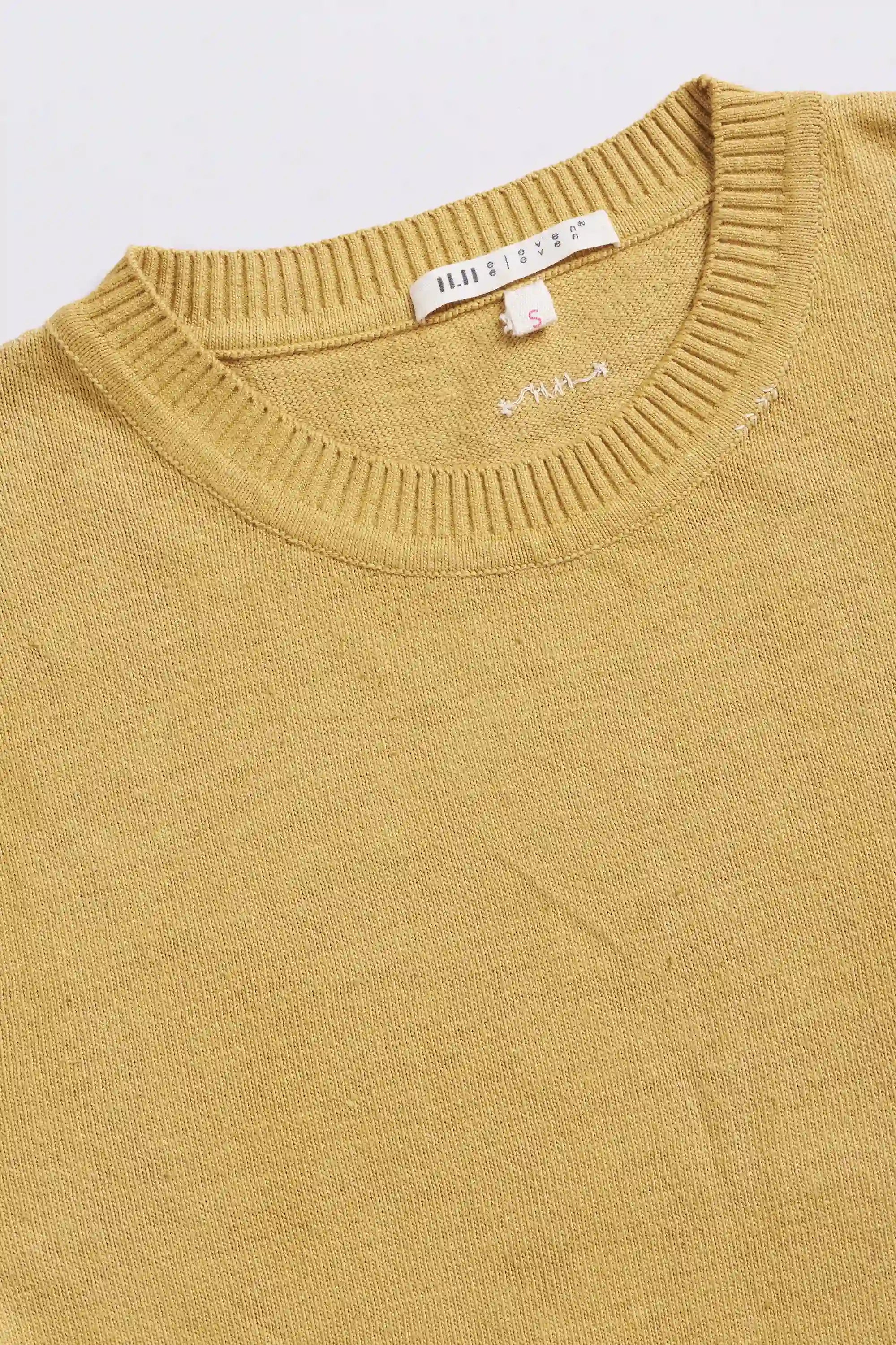 Close-up of a mustard yellow t-shirt with a brand tag on a light gray background