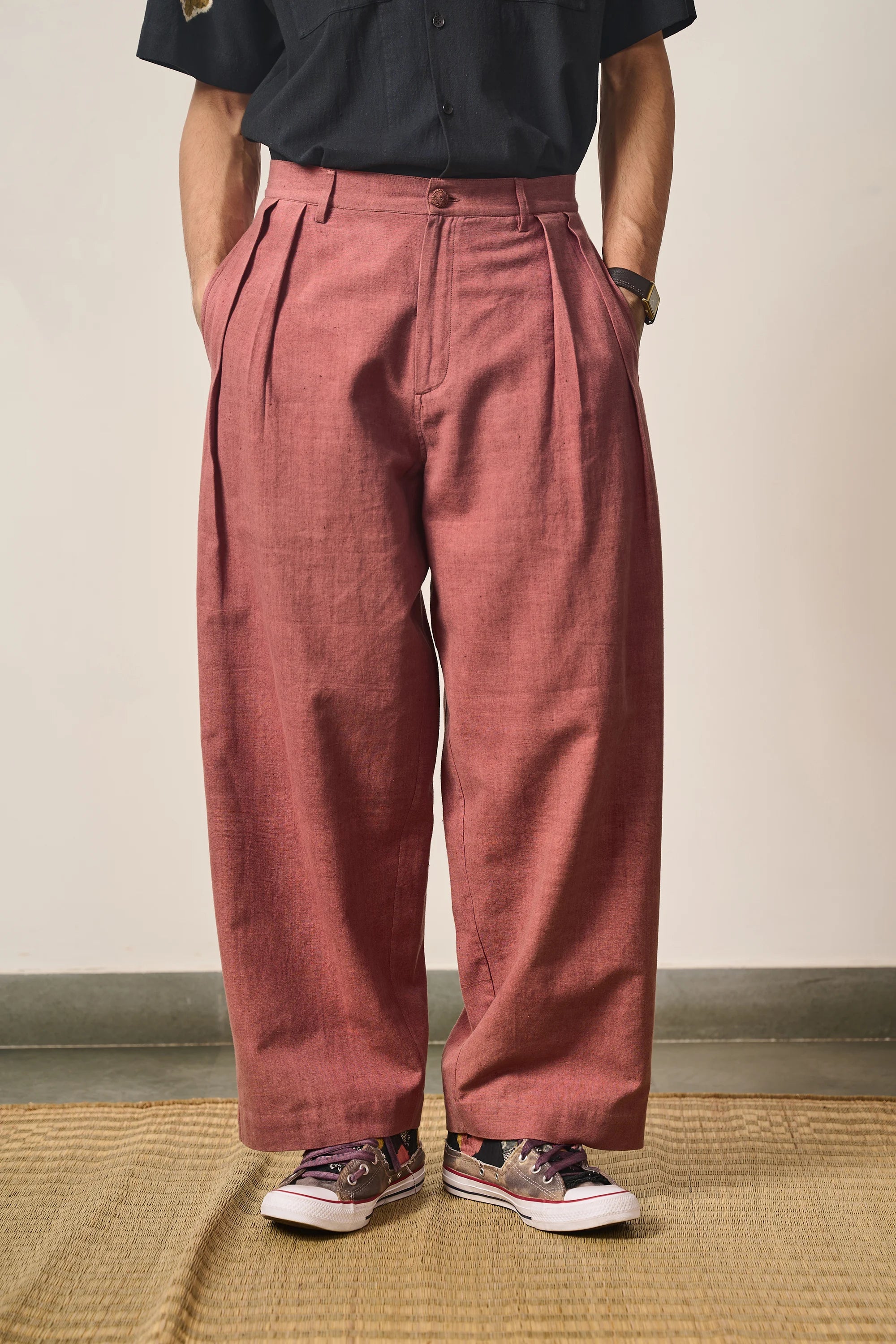 Man wearing Rogue pink pleated pants and a black shirt against a plain background