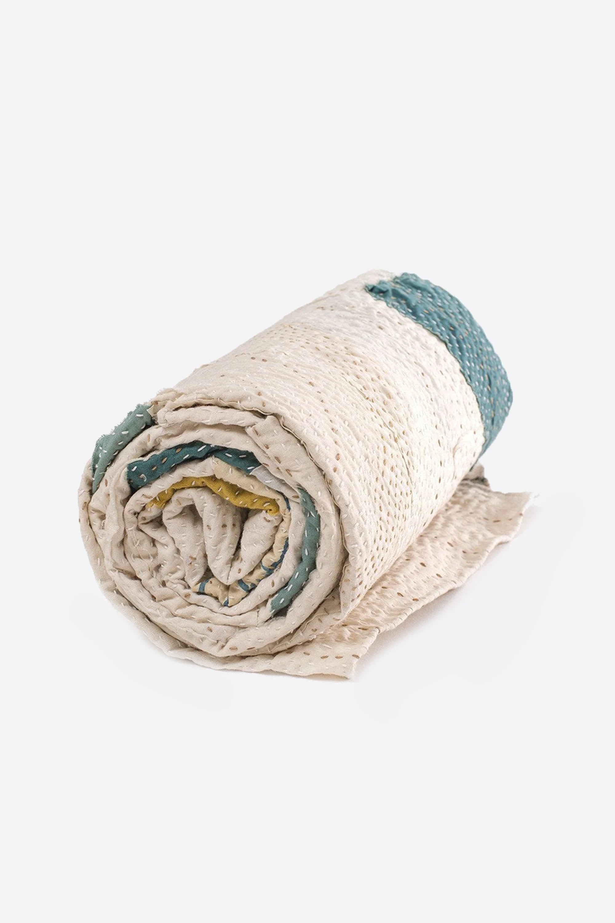 Rolled-up quilt with green and yellow kantha patch work on a grey background