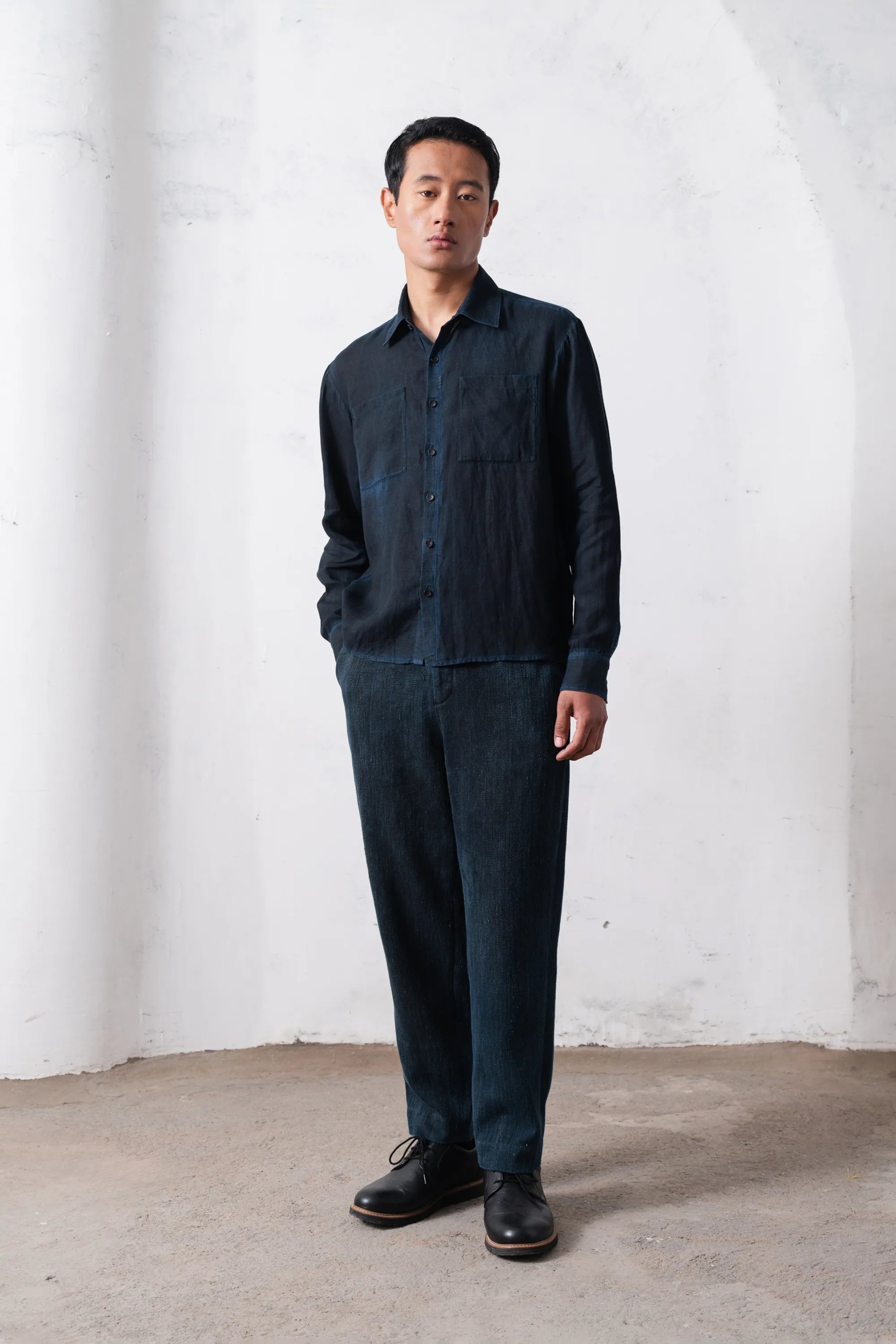 Man wearing a black shirt and pants standing against a white wall