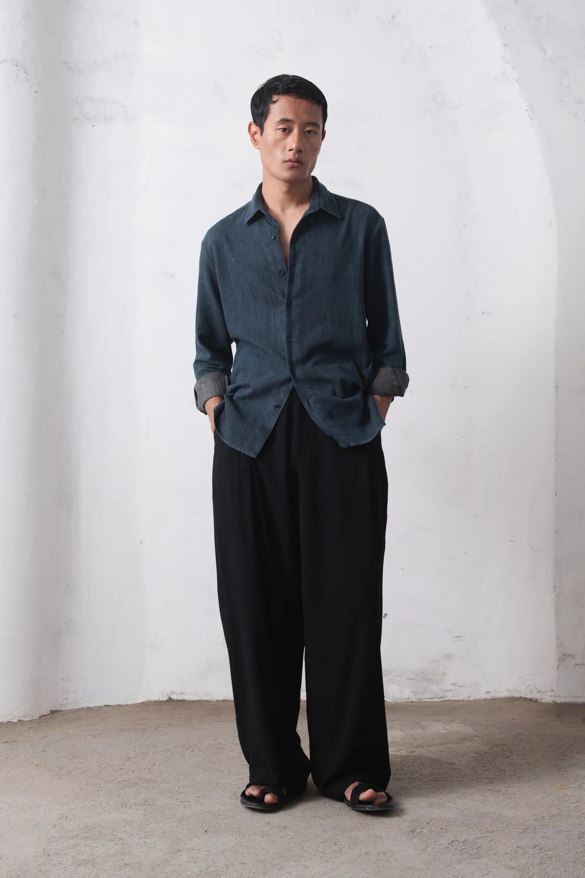 Man wearing a indigo shirt and black pants on a white wall
