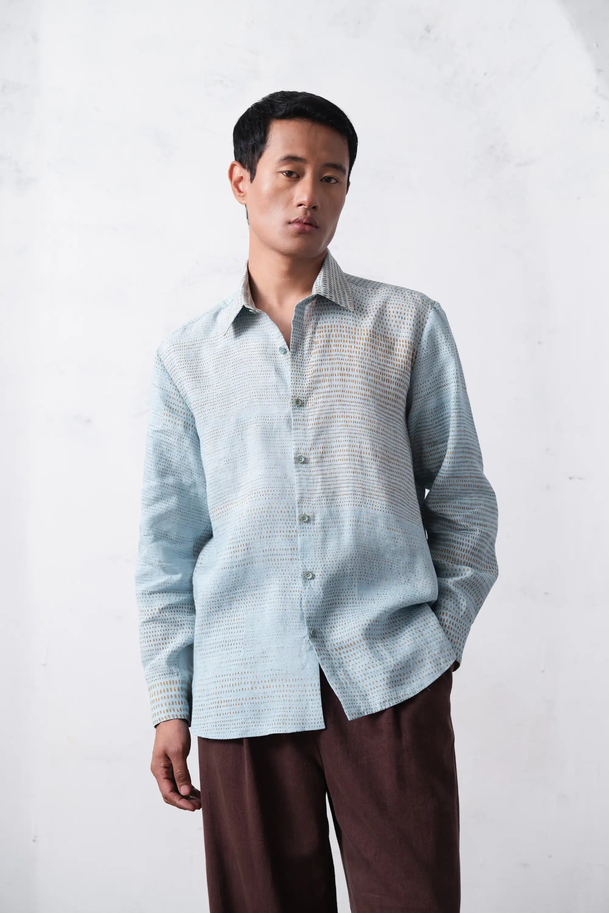 Man wearing a light blue checkered shirt with brown pants against a white background