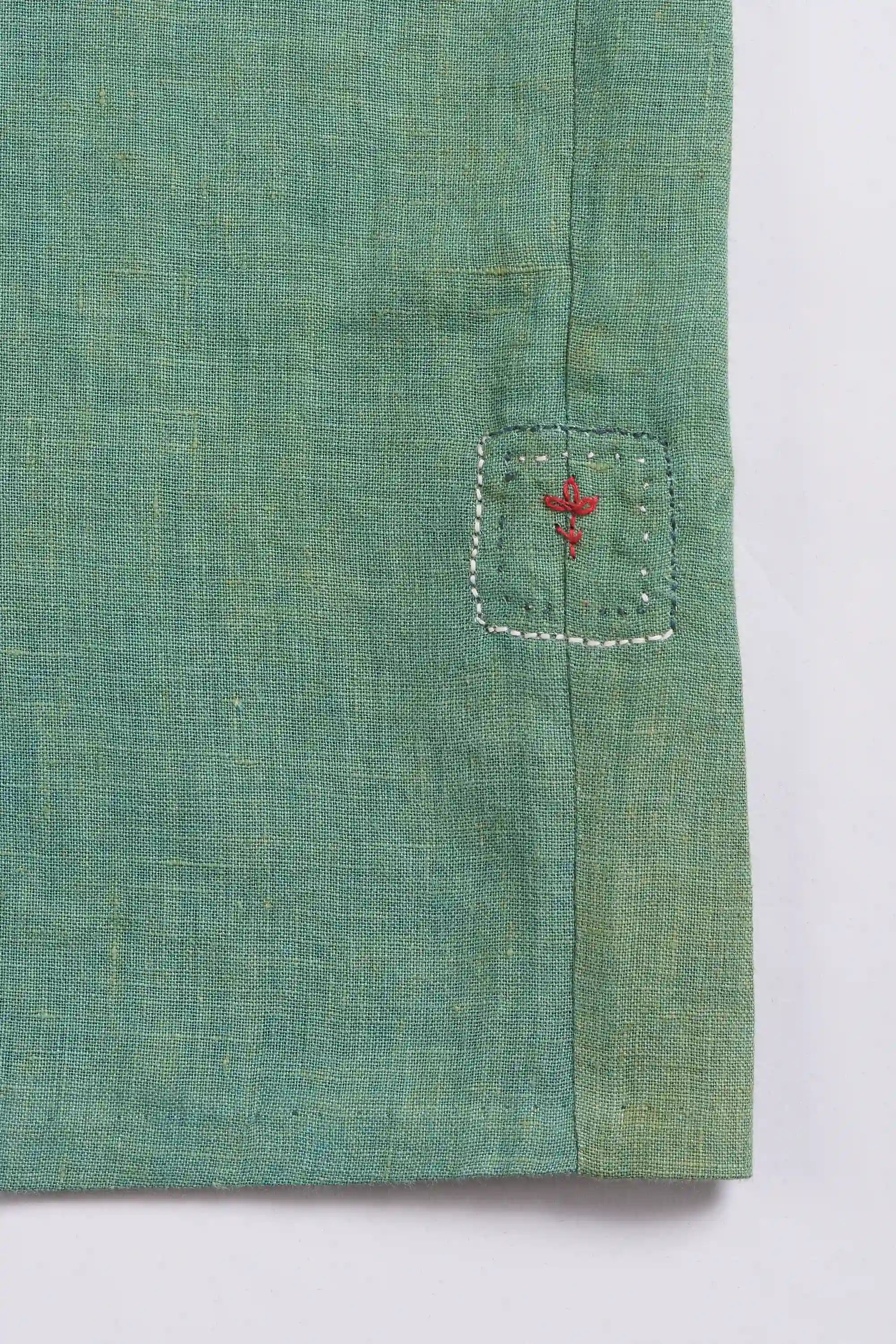 Close-up of green fabric with a small     pehchan on a light grey background 