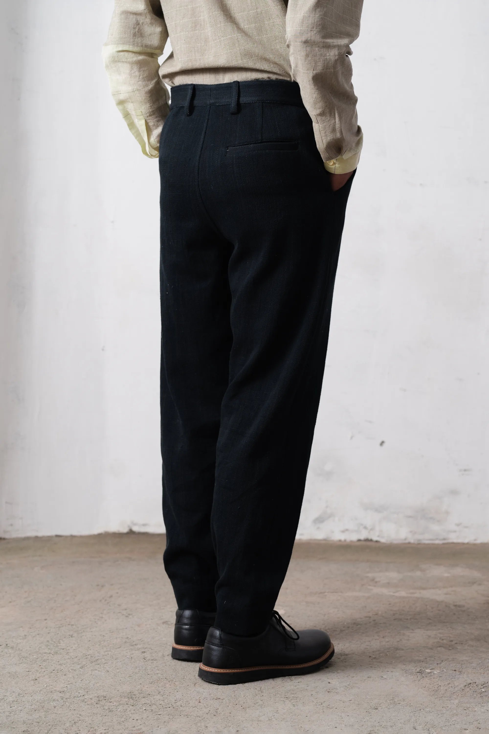 Person wearing black pants and a shirt against a light grey wall