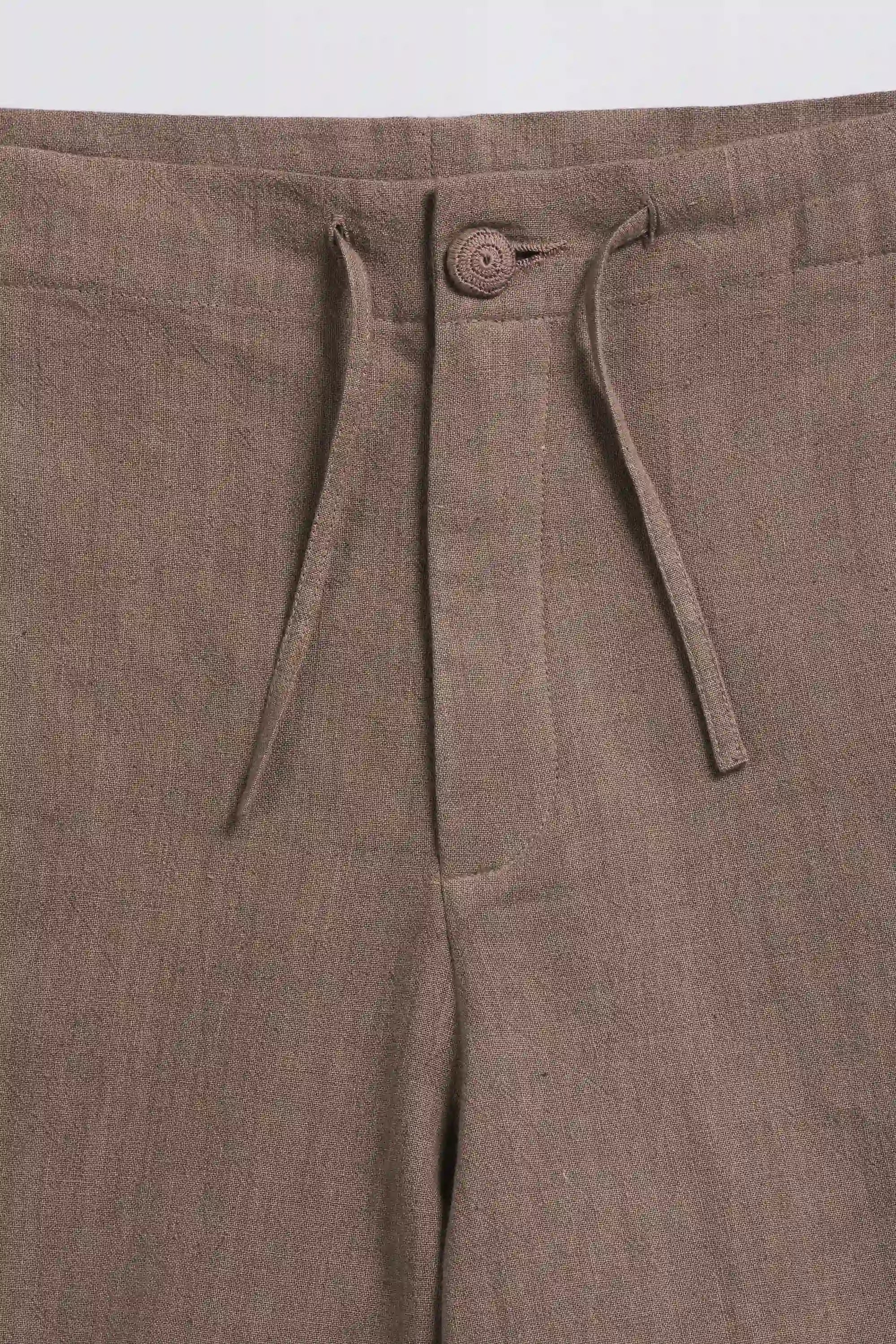 Close-up of brown pants with a button and drawstring on a light grey background