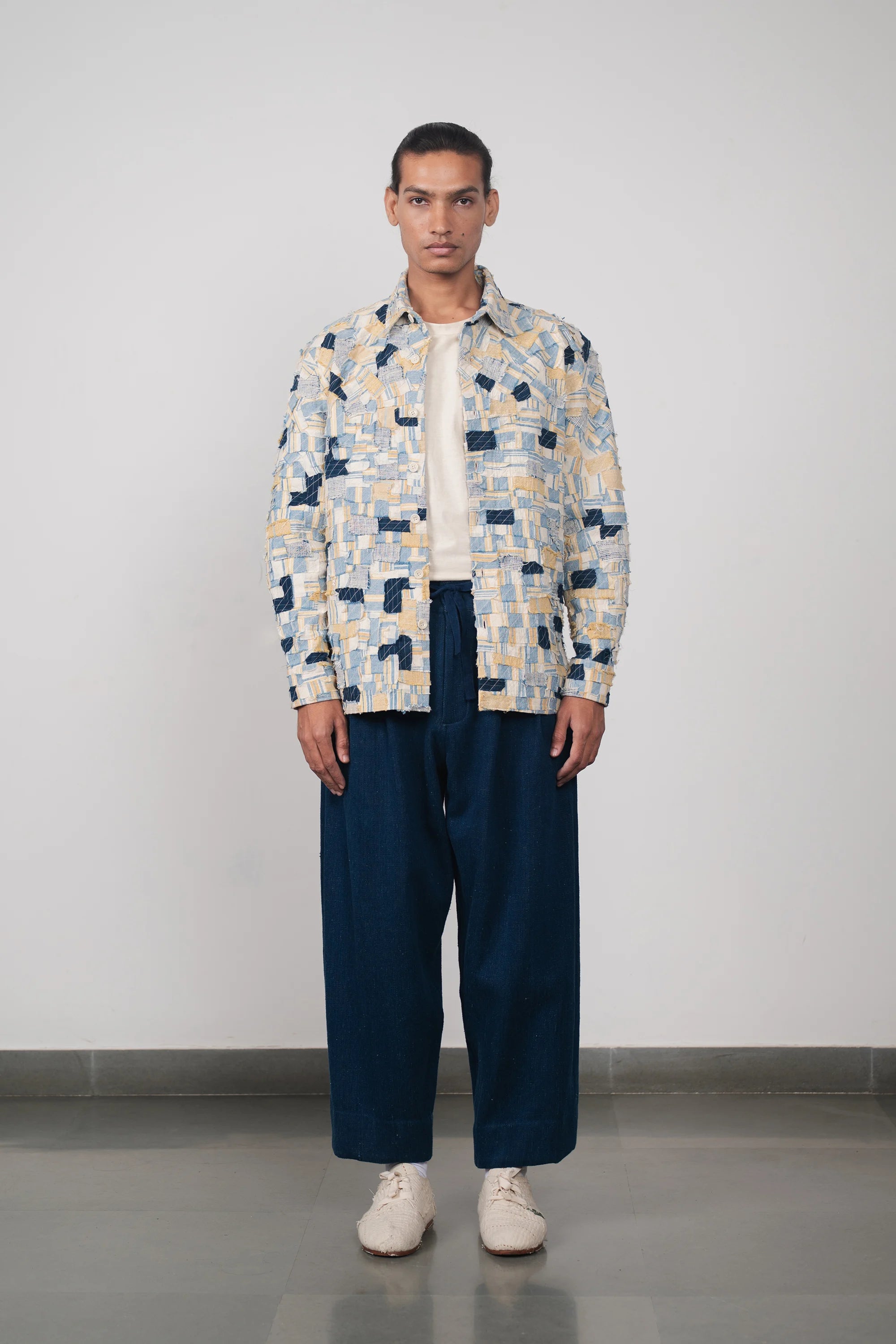 Man wearing a patterned shirt and blue pants against a plain background