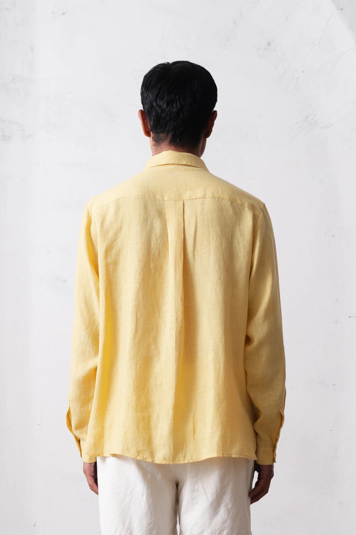 Back shot of a person wearing a light yellow shirt from behind on a light grey background 