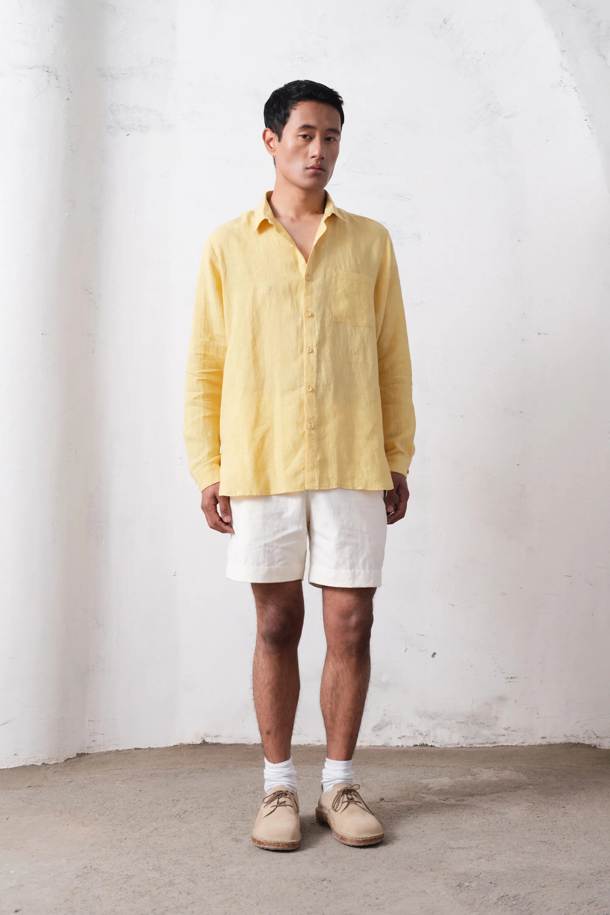 Man wearing a yellow shirt and white shorts against a plain light grey wall