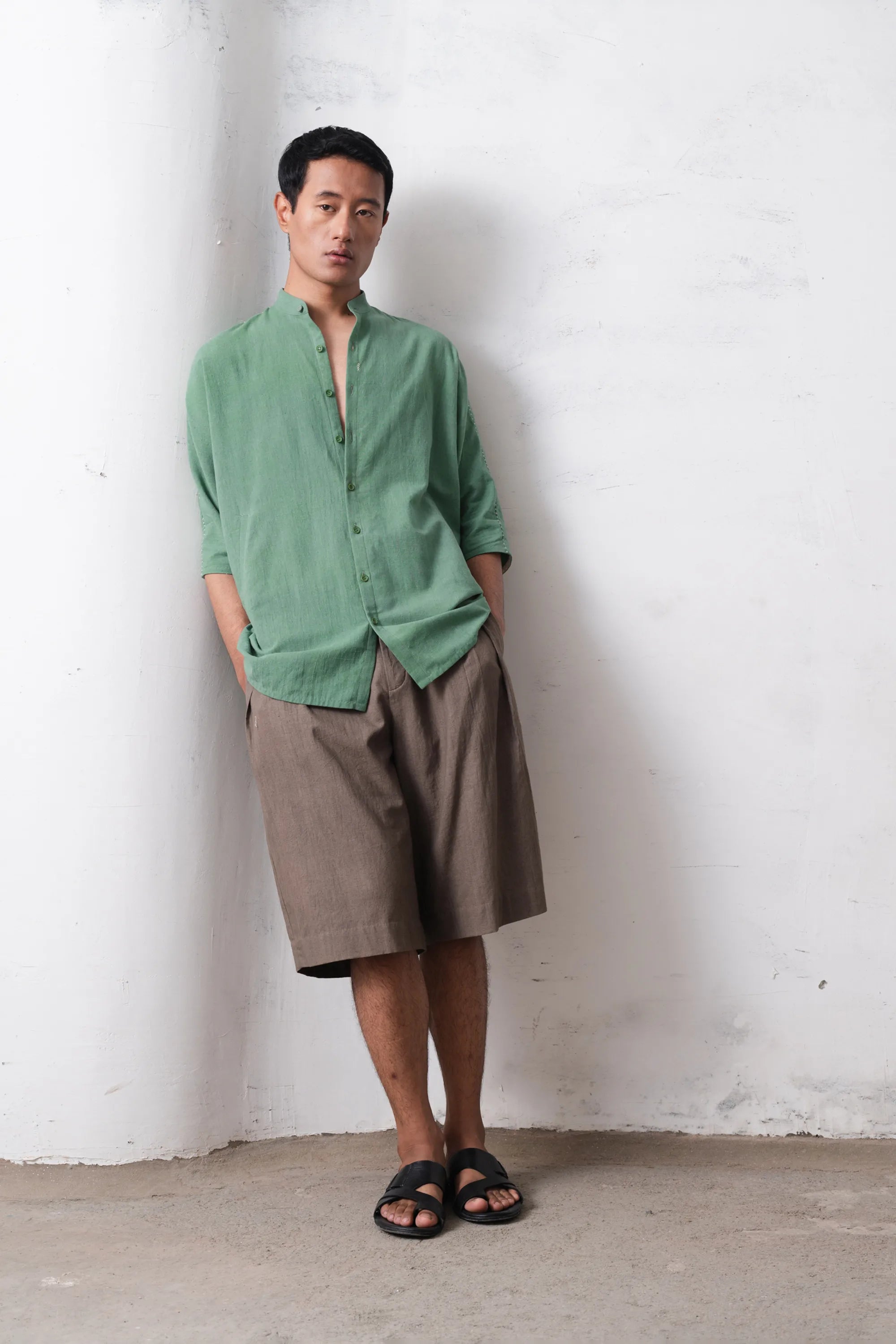 Man wearing a green shirt and brown shorts against a light grey wall