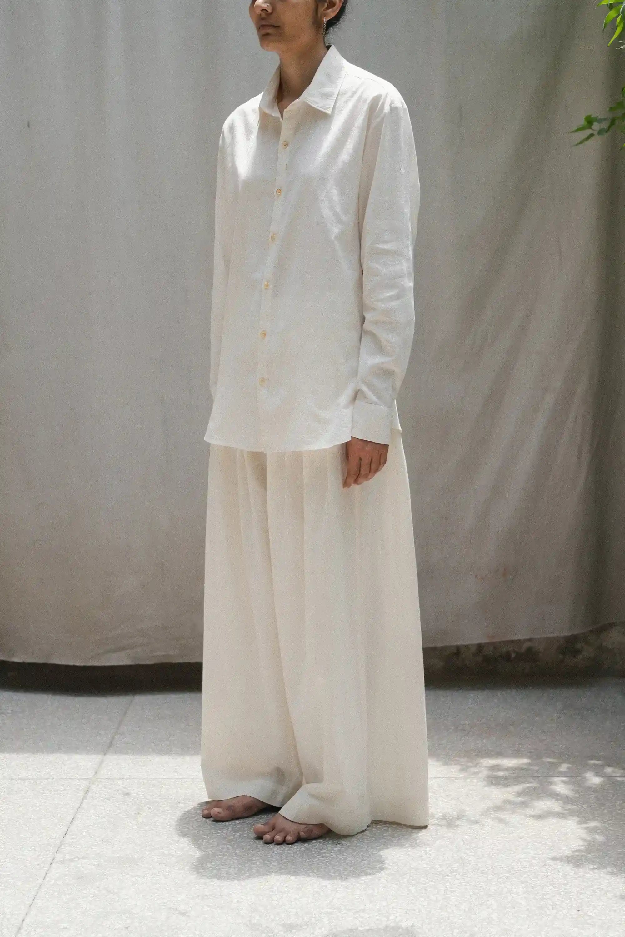 Person wearing a ecru shirt and light-colored pants against a plain background