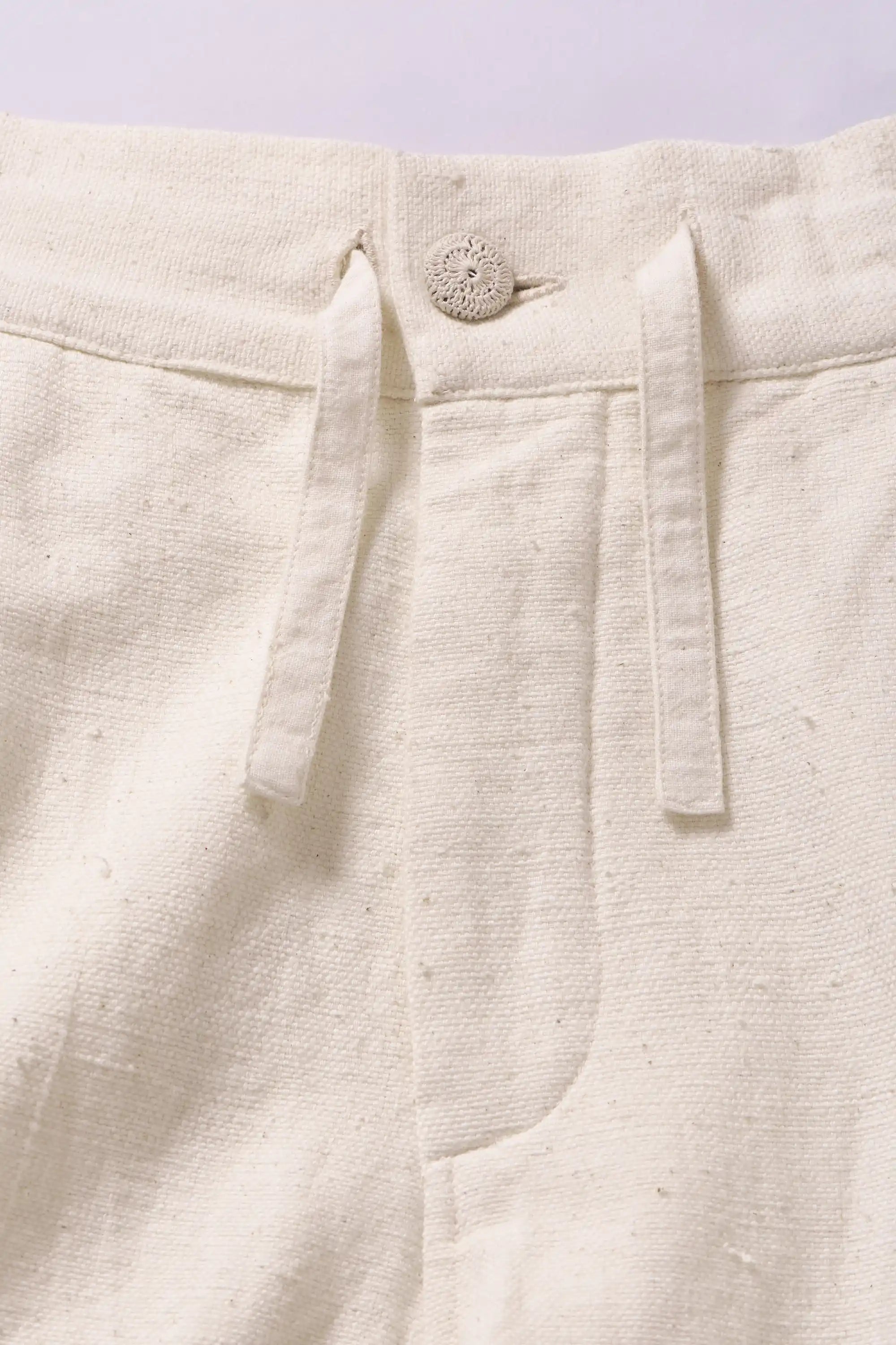 Close-up of ecru pants with a button and strap detail on a light grey background