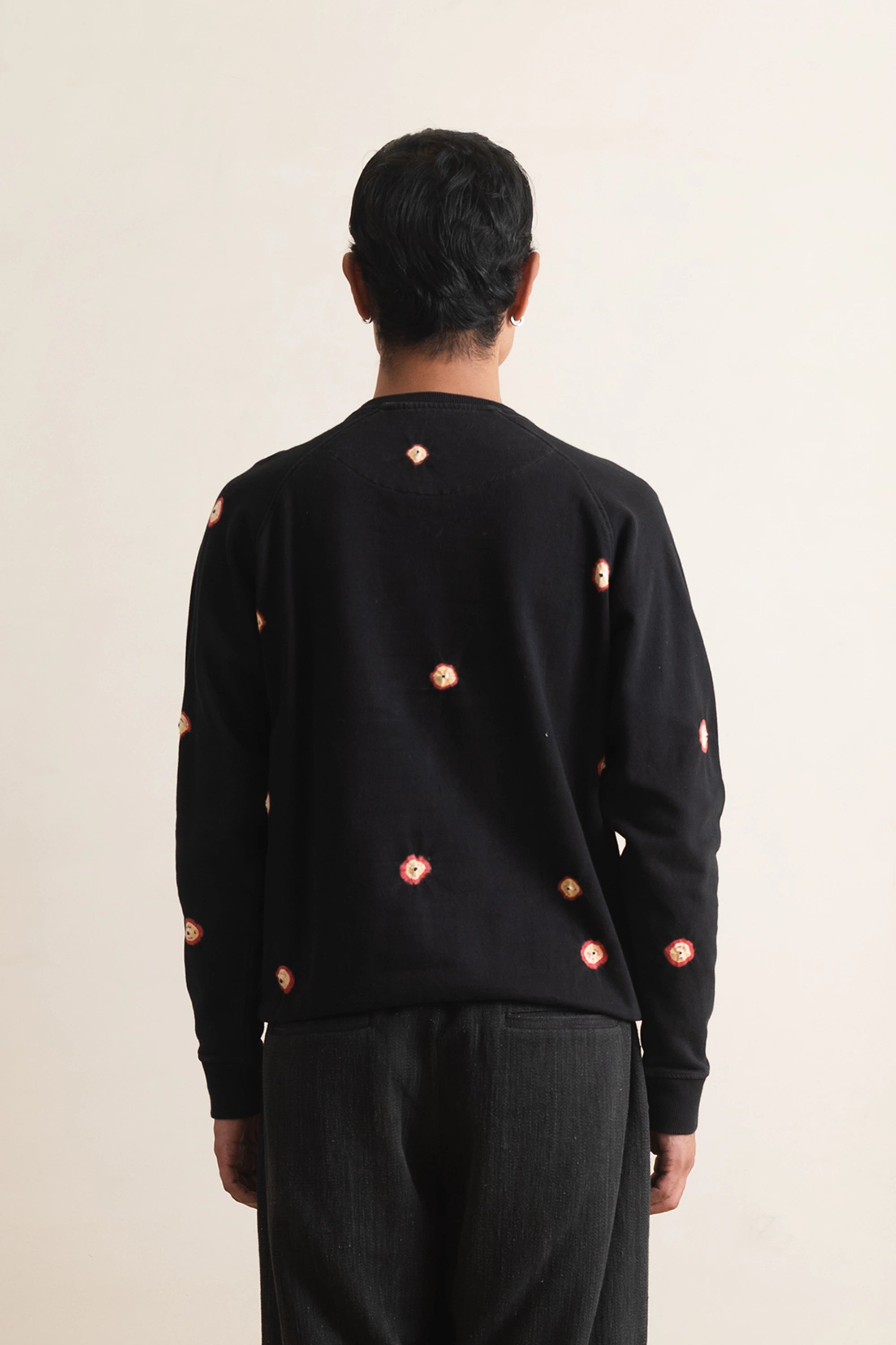 Back shot of a person wearing a black sweatshirt with hand shibori on a light grey background