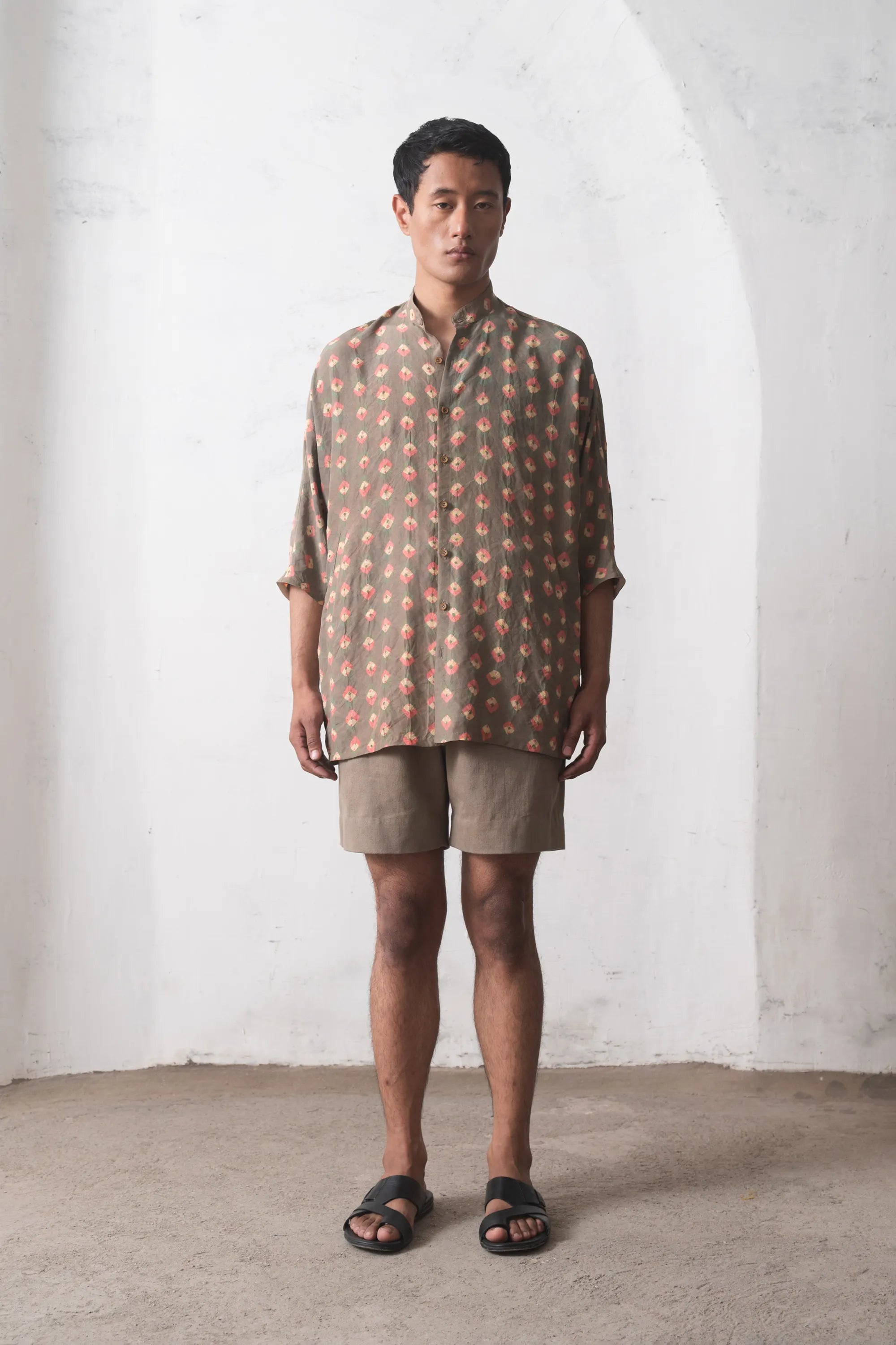 Man wearing a multicolour shirt and beige shorts against a white wall