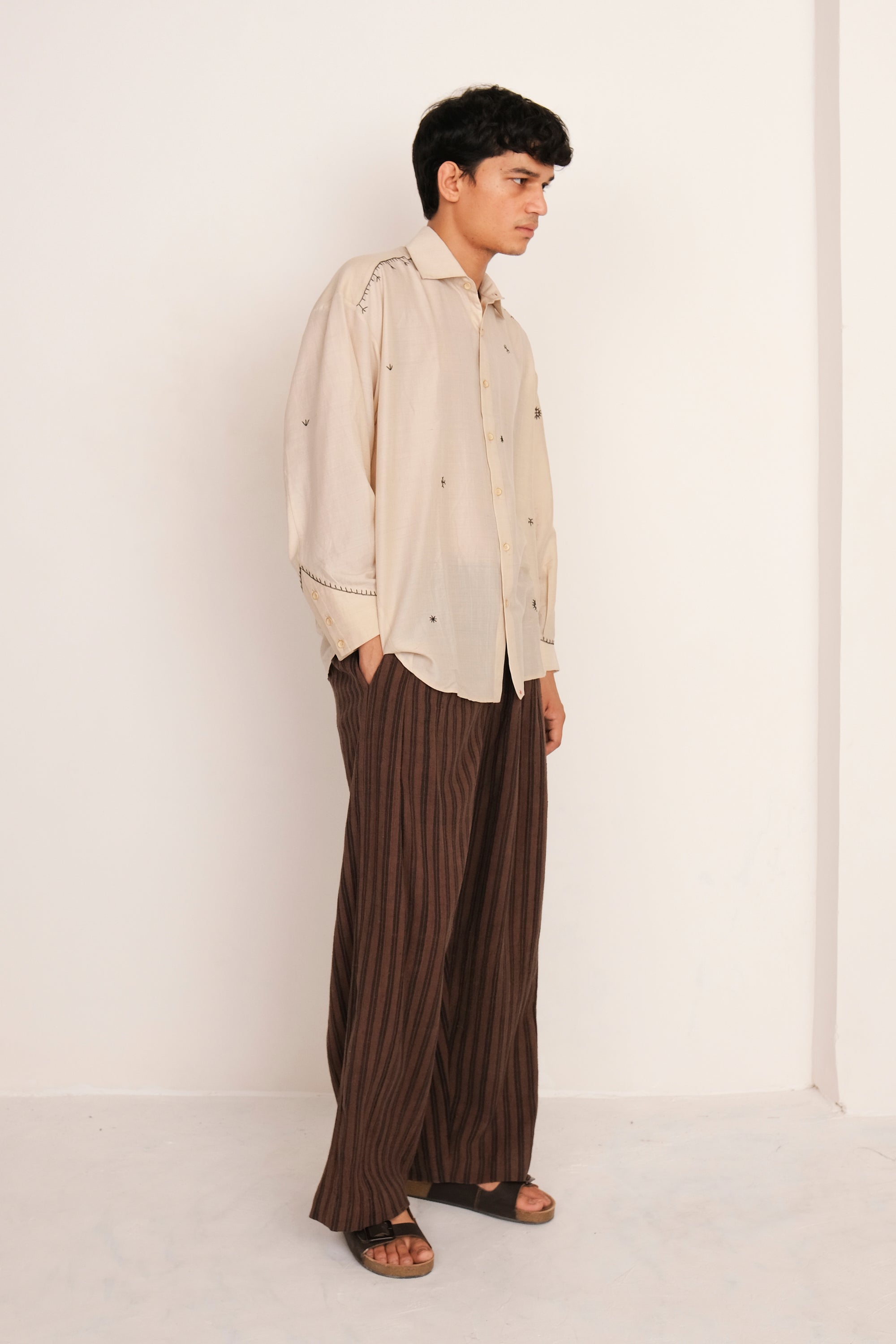 Man wearing a Ecru shirt and burnt umber striped pants against a white background