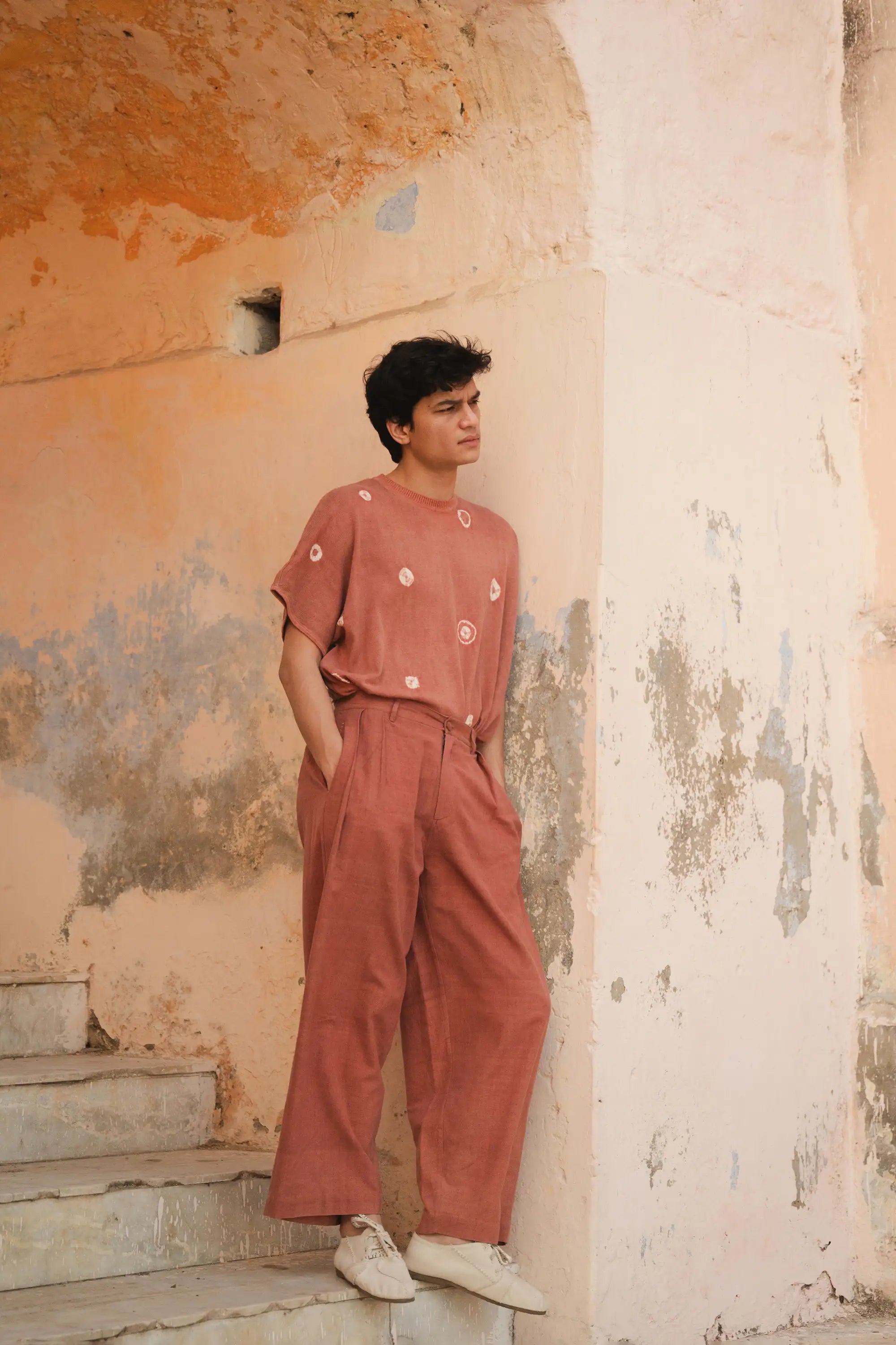 Person wearing a rouge pink cotton t-shirt with hand shibori work with rouge pink pant against a textured wall.