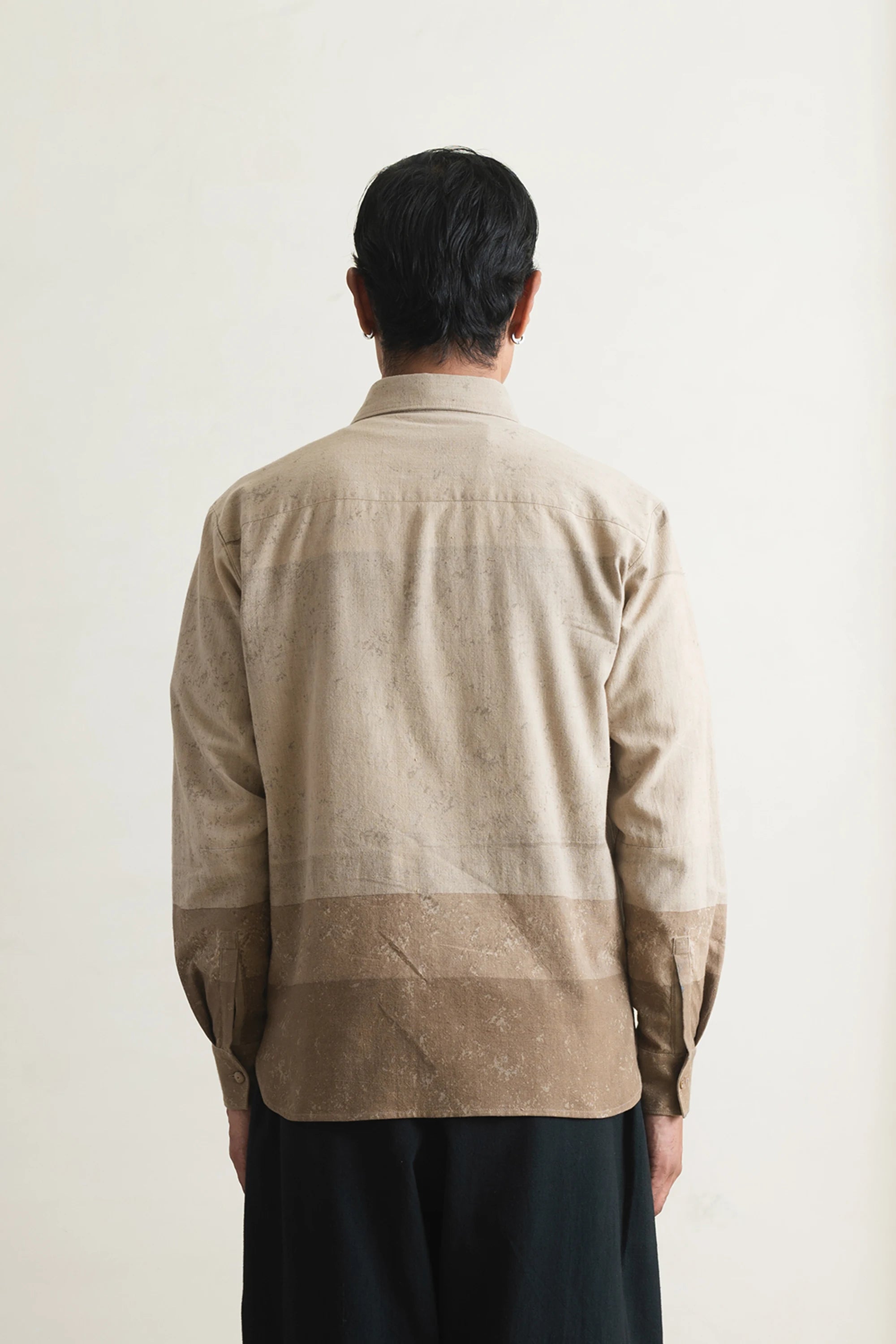 Back shot of a person wearing a beige shirt against a light grey background
