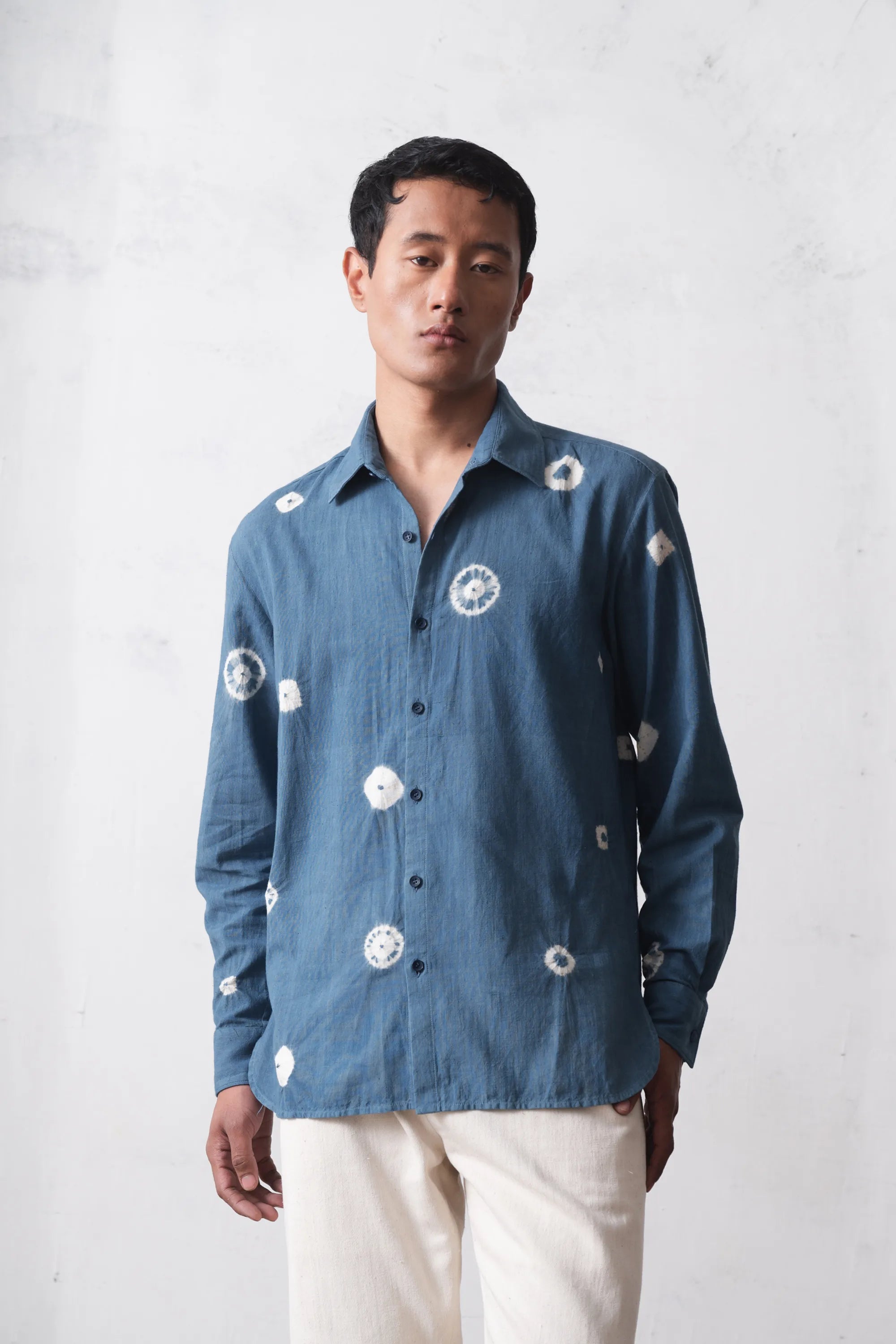 Man wearing a blue cotton shirt with shibori on a light grey background background