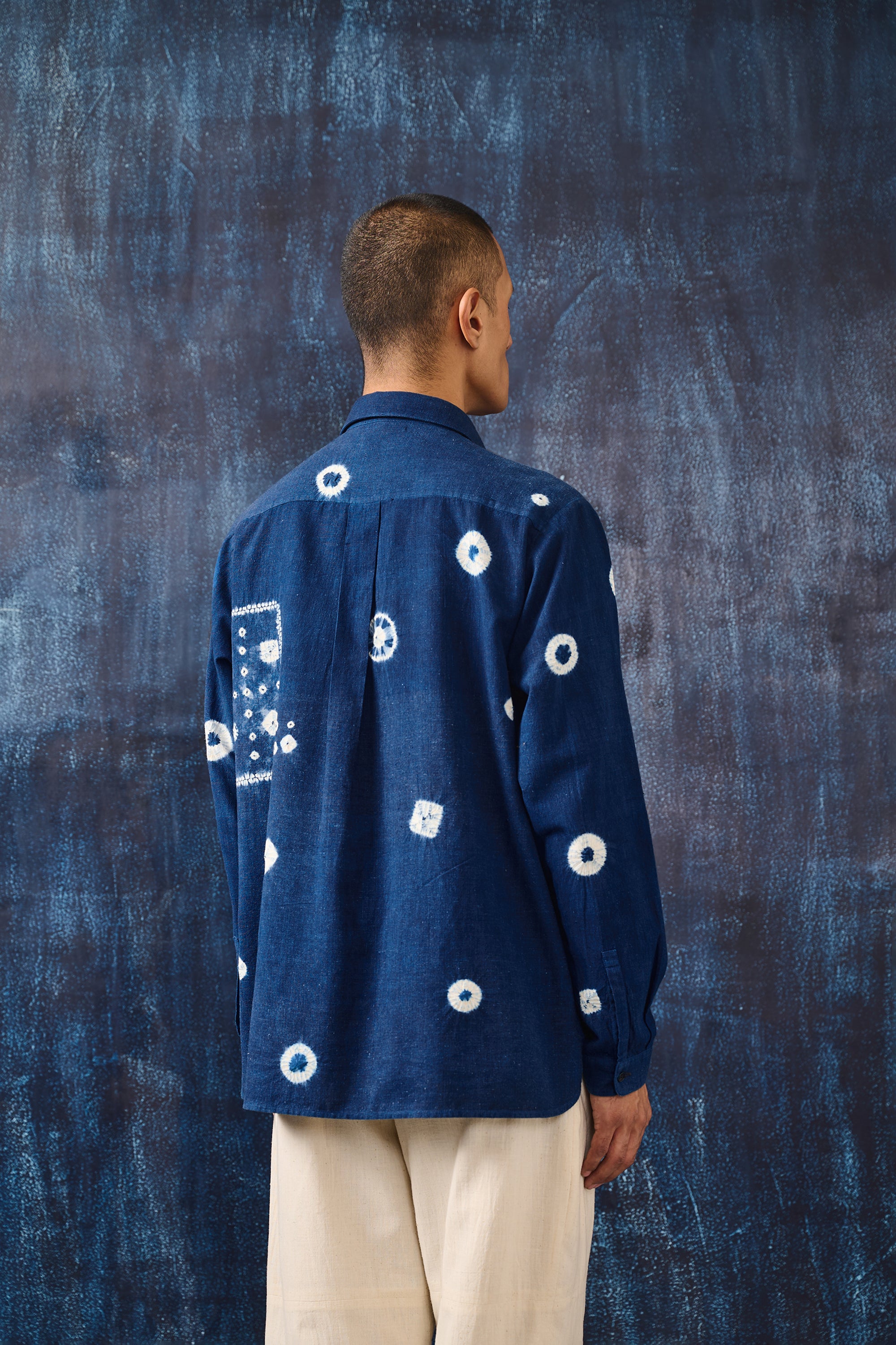 A back shot of a man wearing medium indigo shirt