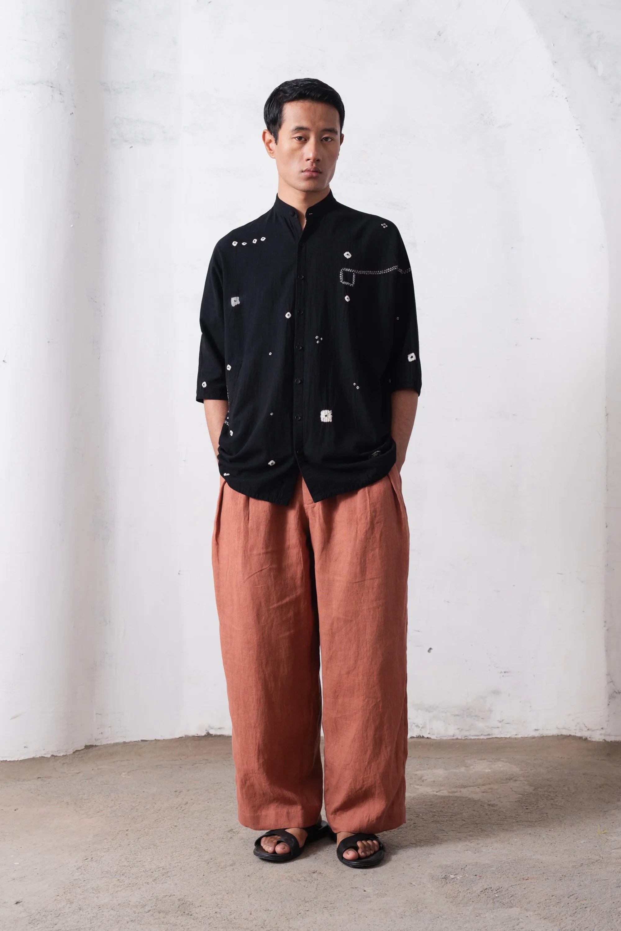 Man wearing a black shirt and orange rust-colored pants against a white wall