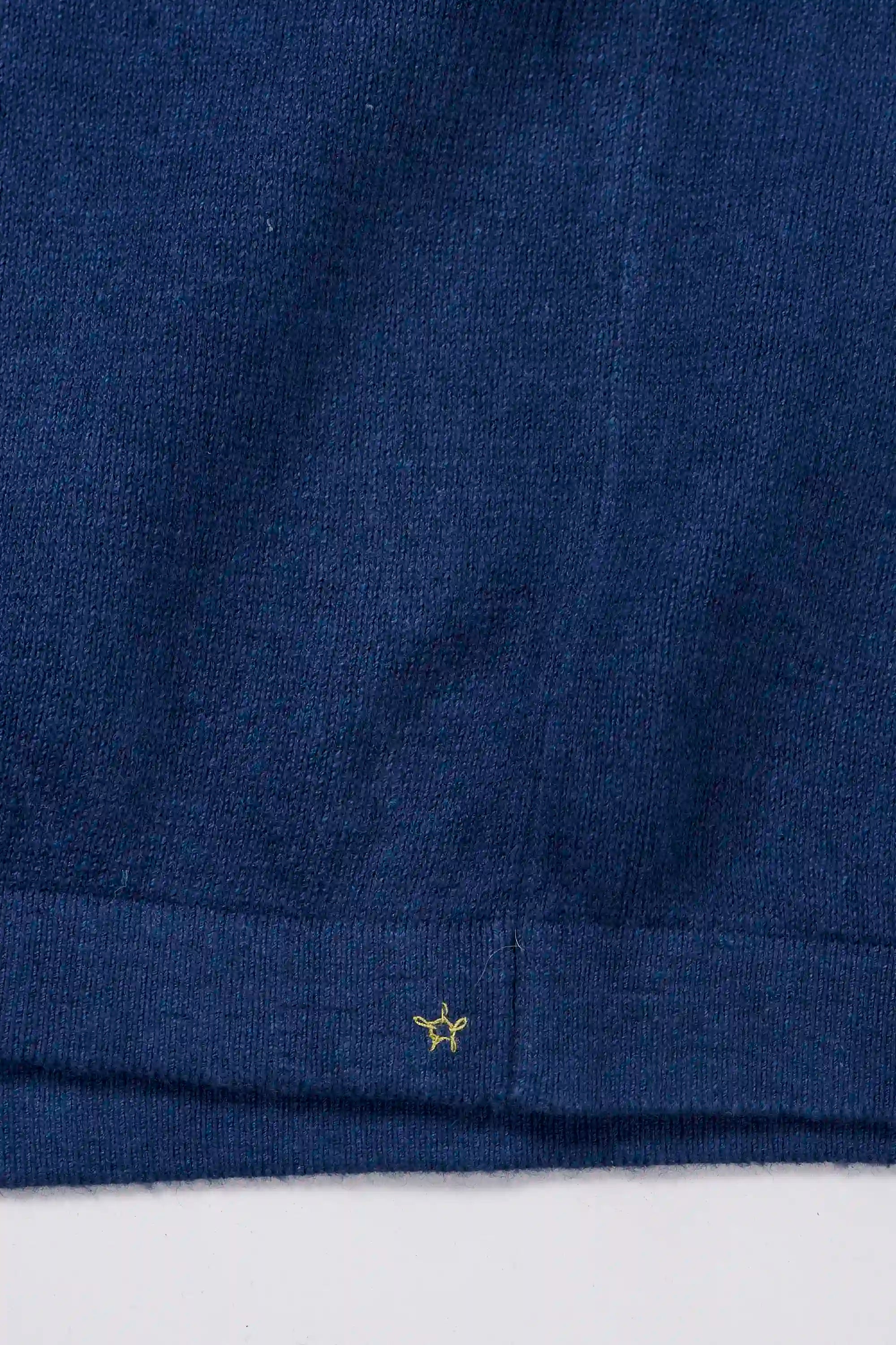 Close-up of a indigo garment with a small yellow hand detail on a grey background