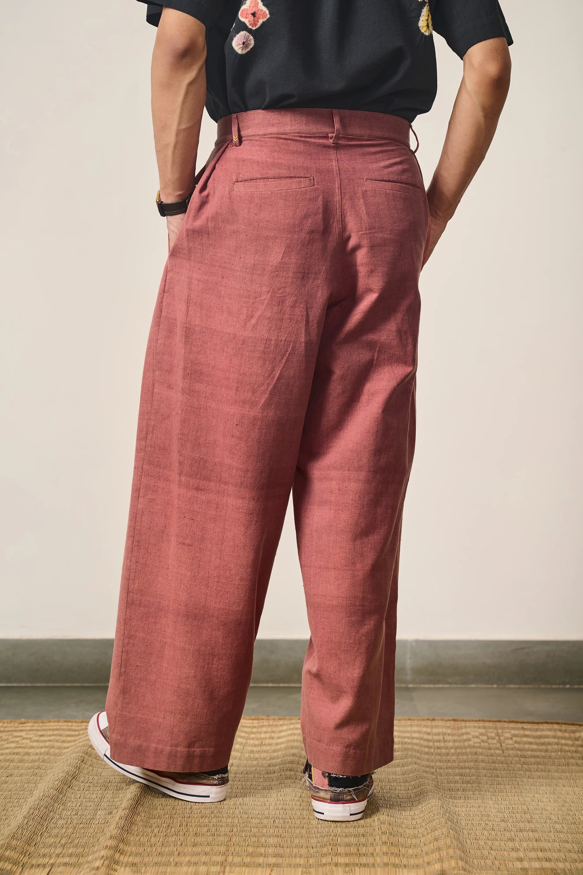 Back shot of man wearing Rogue pink pleated pants and a black shirt against a plain background