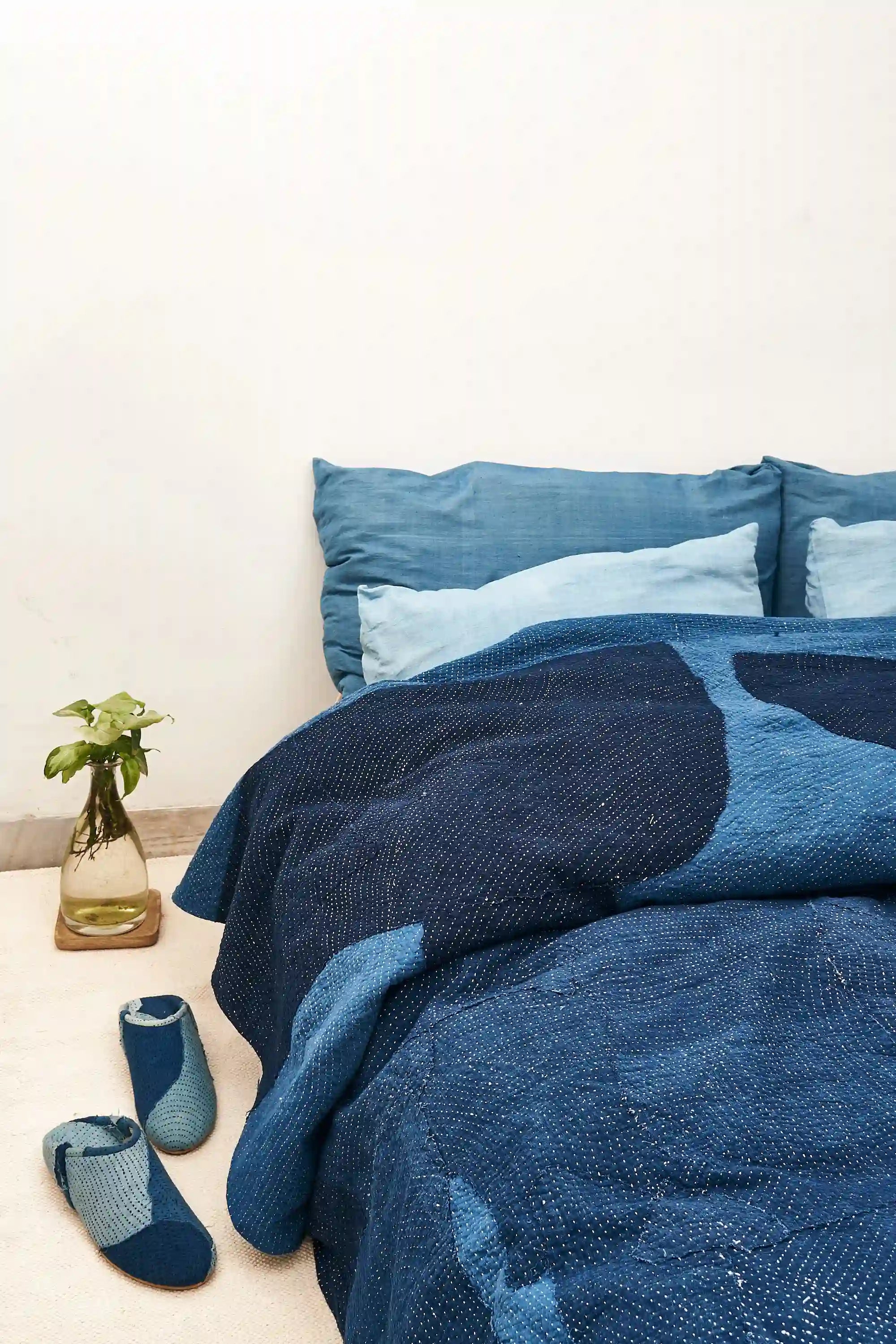 Indigo patterned bedding set on a bed with matching slippers on the floor.